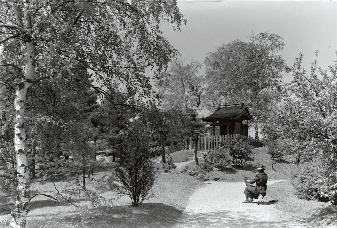 Archival photo of a woman sitting in a garden path, sketching the landscape.
