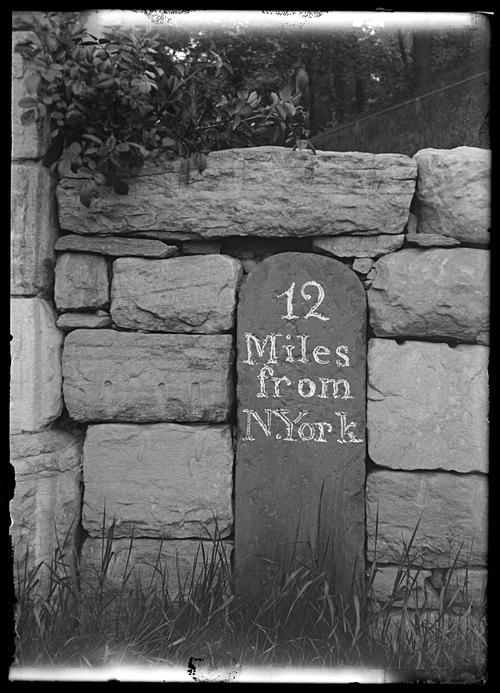 A mile marker reading "12 Miles from N. York" is embedded in a stone wall.