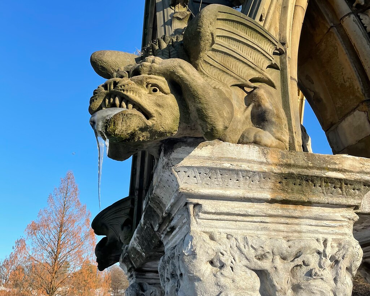 An icicle drips from the fanged, grimacing, toothy maw of a winged stone monster.