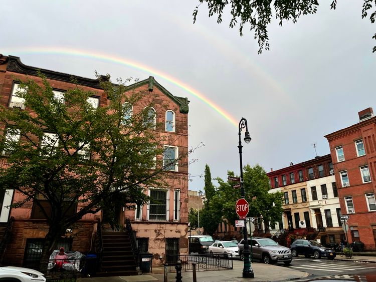 A rainbow's arc just clears the roof of a corner Brooklyn brownstone.