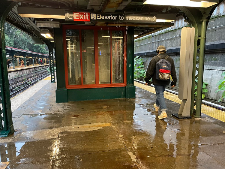 A man walks along a partially covered outdoor subway platform. The floor is all puddles.