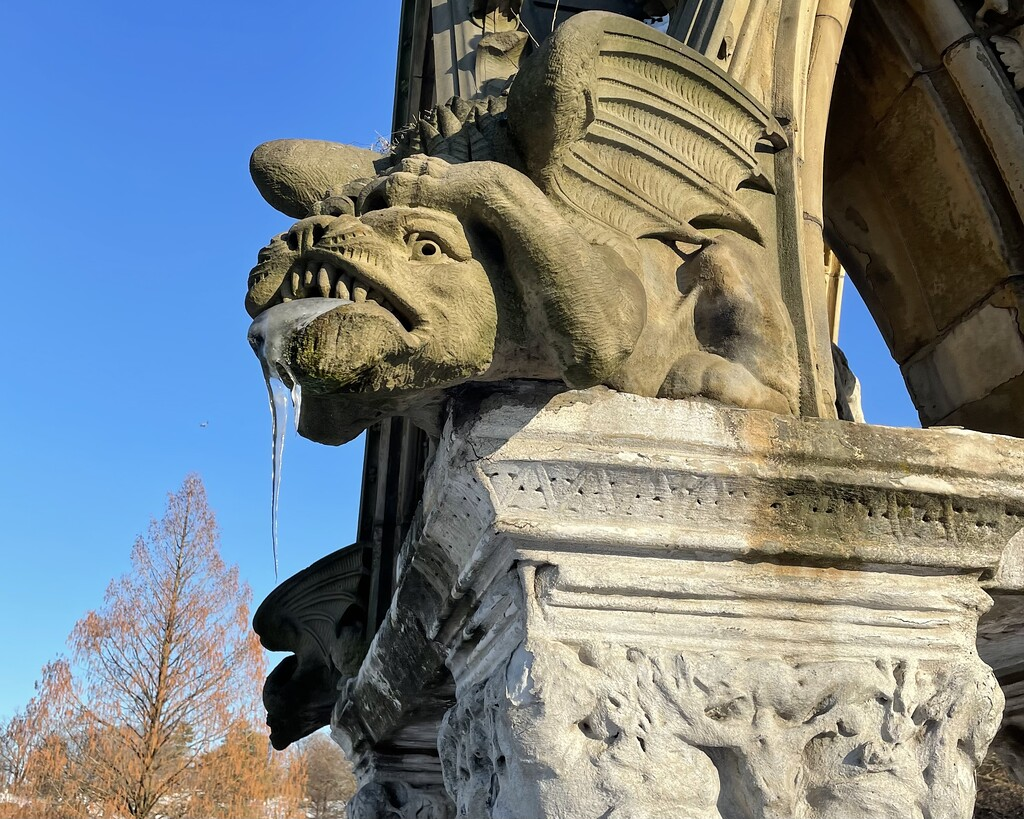 An icicle drips from the fanged, grimacing, toothy maw of a winged stone monster.